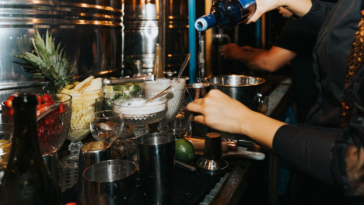 Licensed event bartender pouring a spirit at a fully stocked cocktail bar
