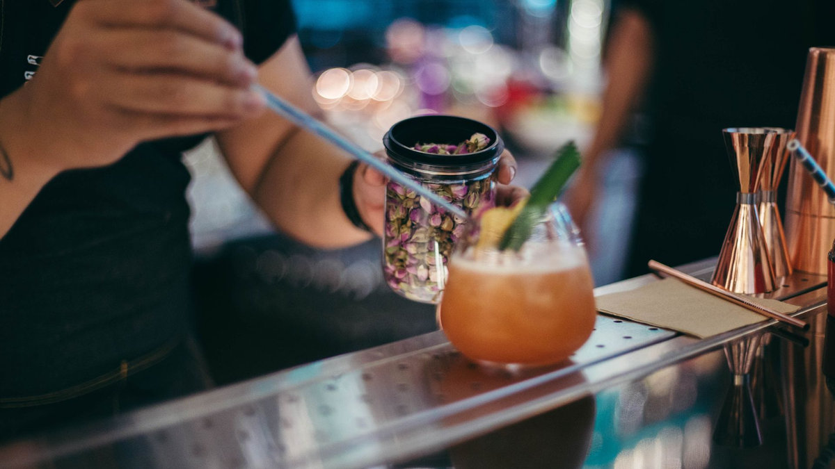 Certified bartender garnishing a craft cocktail with dried rose petals