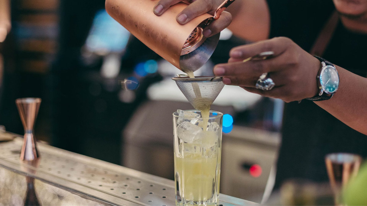 Insured event bartender fine-straining a fresh cocktail over ice
